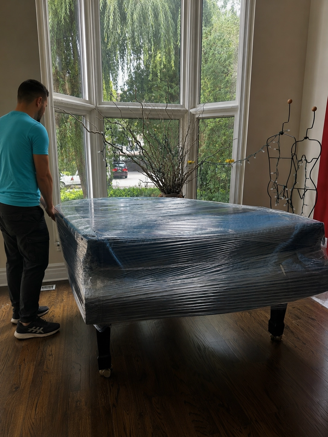 Mover moving a shrink-wrapped grand piano across a living room